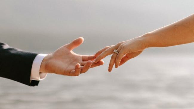 Close-up of a couple's hands showcasing wedding rings by the waterfront.